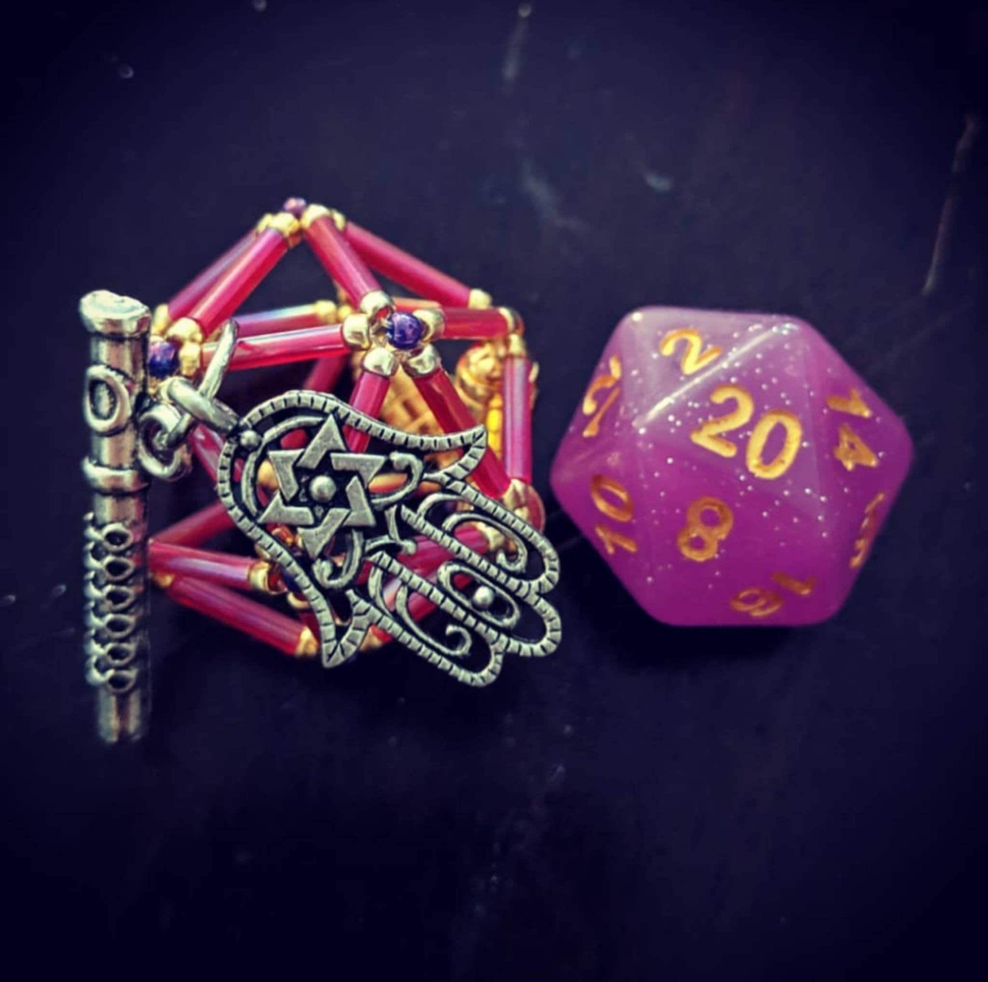 Scanlan necklace: pink, gold flower D20 cage with purple accent beads. Two charms: flue and hand.