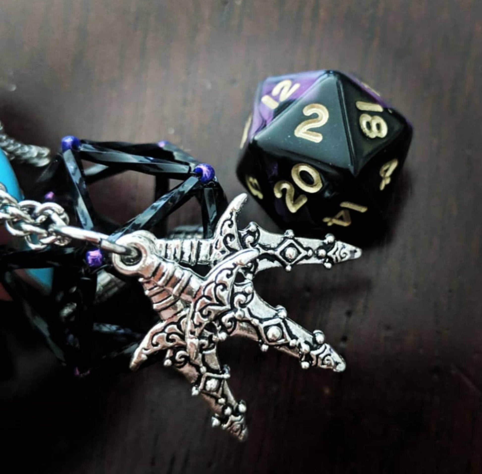 Vax necklace: Black and purple D20 cage with three dagger charms.