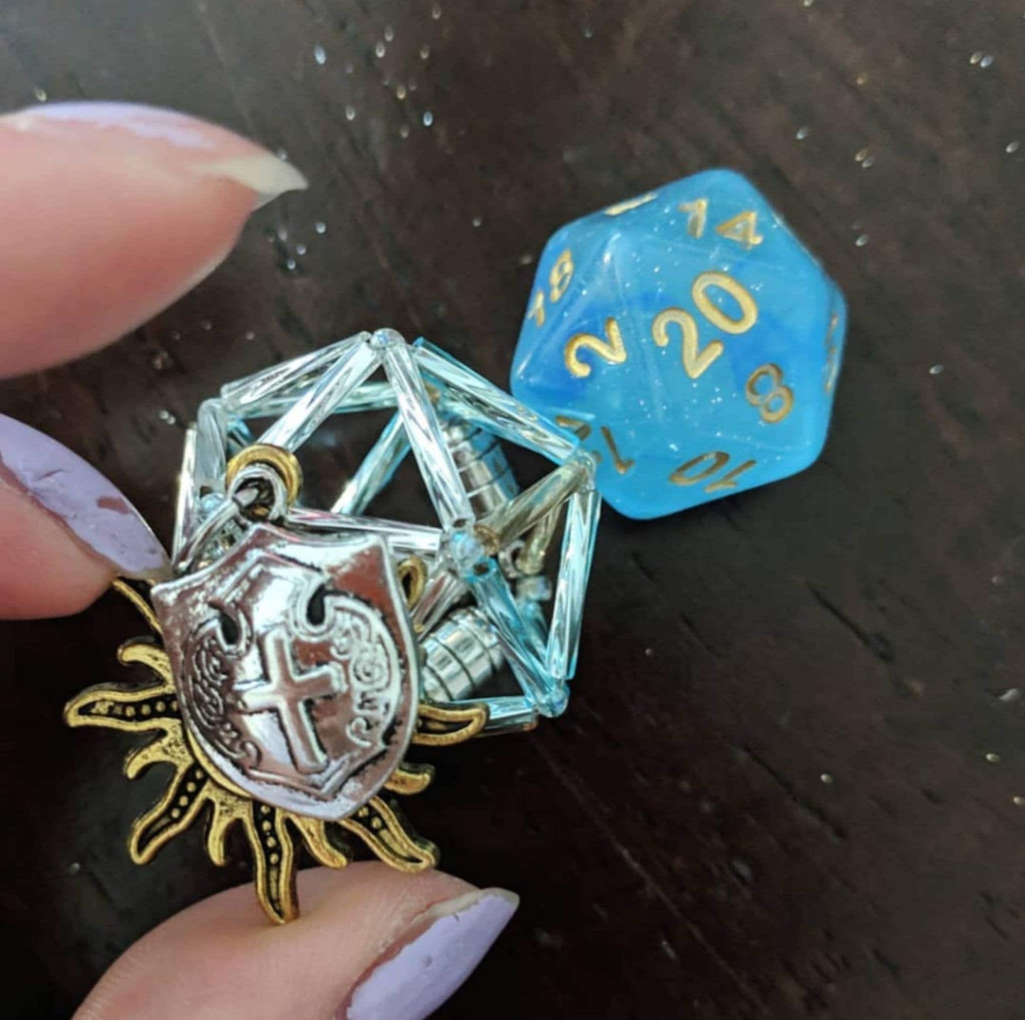 Pike necklace: silver and light blue D20 cage with two charms. A golden sun and silver shield.