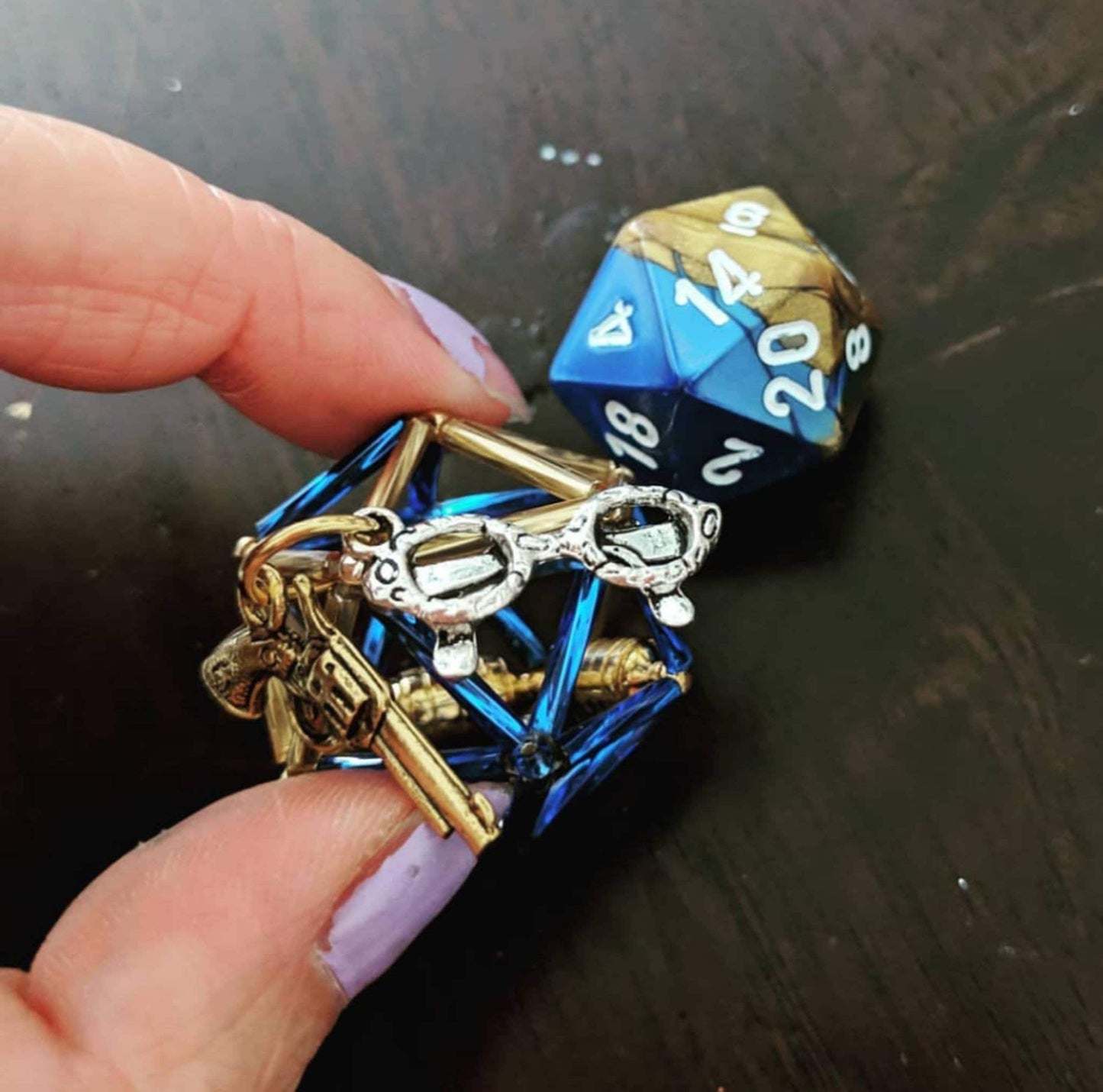 Percy necklace: gold and blue D20 and cage with two charms: gold gun and silver glasses.