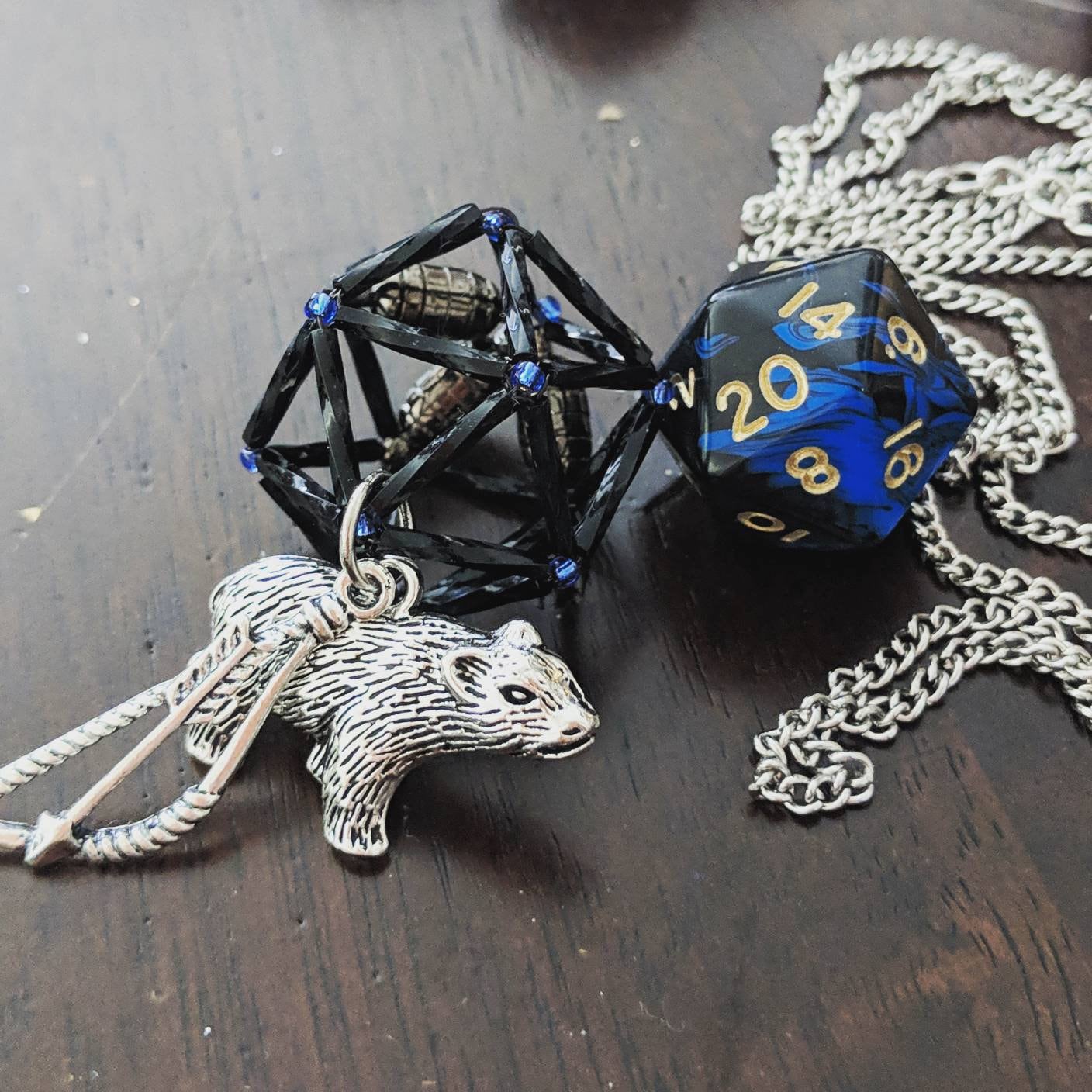 Vex Necklace: Black necklace cage with blue accent beads. Two charms: bow and arrow and bear charm.